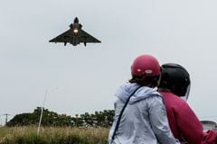 Dos personas viajan en motocicleta mientras un avión de combate Mirage 2000 de la Fuerza Aérea de Taiwán se acerca para aterrizar en una base de la fuerza aérea en Hsinchu, en el norte de Taiwán, el 23 de mayo de 2024.