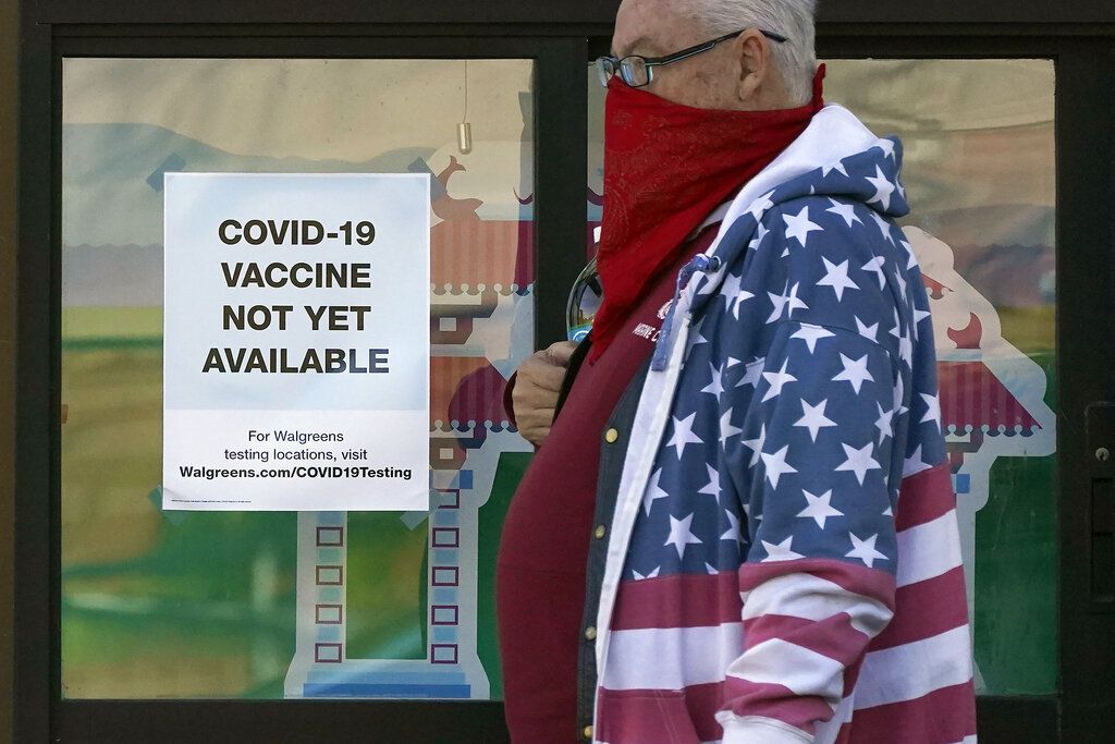A pedestrian wearing a mask walks past a sign advising that COVID-19 vaccines are not available yet at a Walgreen's pharmacy store during the coronavirus outbreak in San Francisco, Wednesday, Dec. 2, 2020. (AP Photo/Jeff Chiu)
