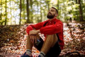 Retrato de joven relajado con auriculares bluetooth en el bosque