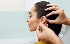 Instalación de audífonos en el oído de la mujer en la clínica auditiva, primer plano, vista lateral. Tratamiento de la sordera, soluciones auditivas