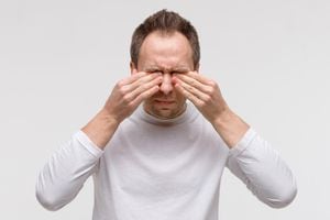Cerca del hombre tiene un problema con las lentes de contacto, frotándose los ojos hinchados debido al polen, alergia al polvo. Síndrome del ojo seco, lagrimeo, prurito. Aislado sobre fondo gris, vista frontal. Tic Nervioso