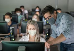 Profesor que llevaba una mascarilla y ayudando a la alumna a una clase de TI - educación durante la pandemia COVID-19