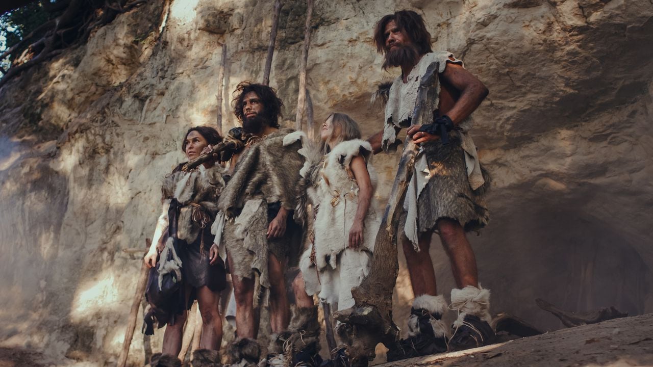Tribu de cazadores-recolectores que llevan piel de animal sosteniendo herramientas de piedra con puntas.