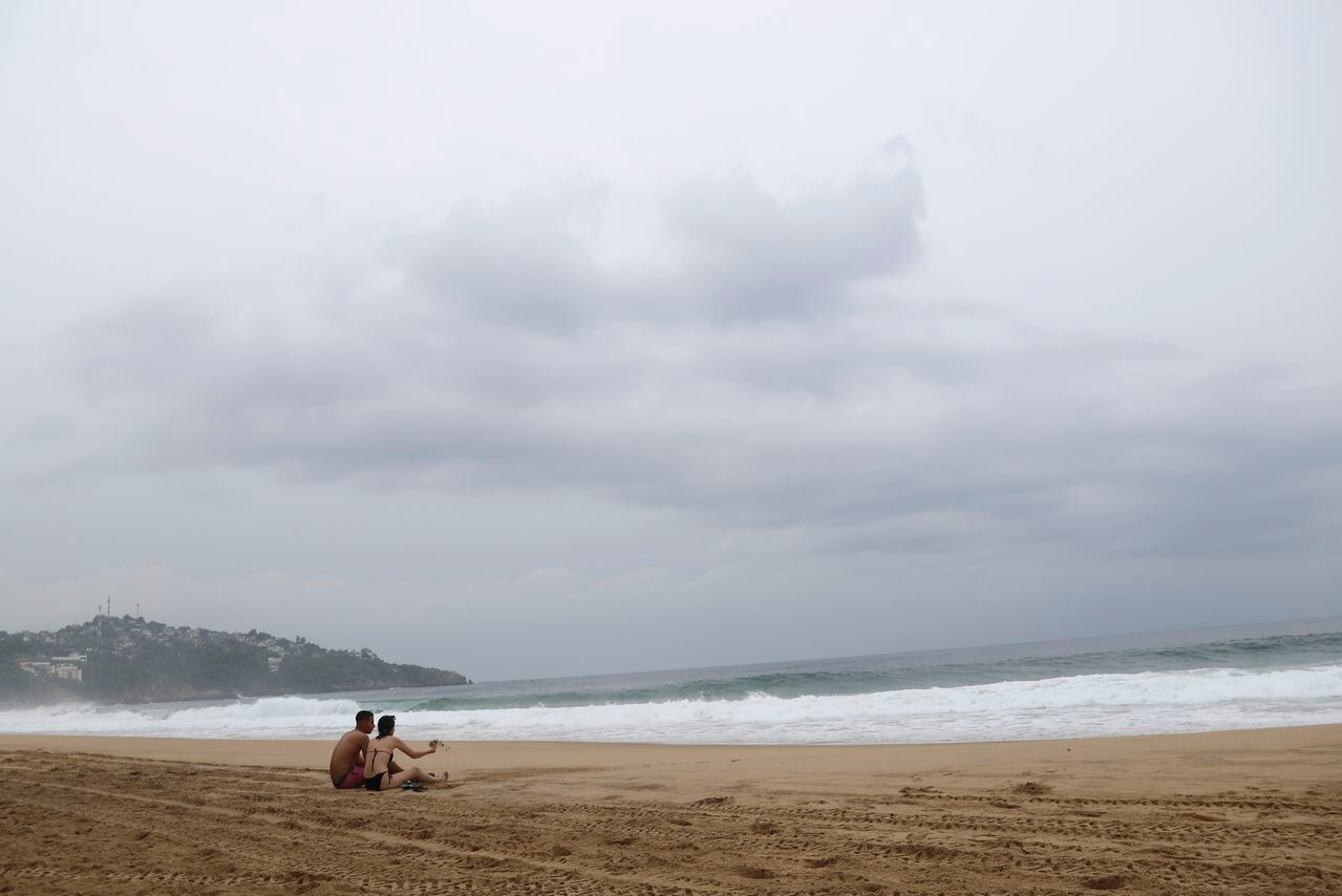Turistas se sientan en la playa en Acapulco, México, el martes 24 de octubre de 2023. El huracán Otis se ha fortalecido de tormenta tropical a huracán de categoría mayor en cuestión de horas a medida que se acerca a la costa del Pacífico sur de México, donde se pronosticaba que tocaría tierra cerca del centro turístico de Acapulco temprano el miércoles. (Foto de AP/Bernardino Hernández)