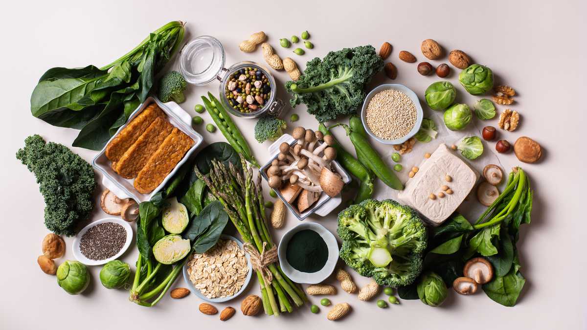 Variedad de alimentos veganos saludables, fuentes de proteínas a base de plantas y alimentos para la construcción del cuerpo. Tofu soja tempeh, vegetales verdes, nueces, semillas, harina de avena con quinua y espirulina. Vista desde arriba