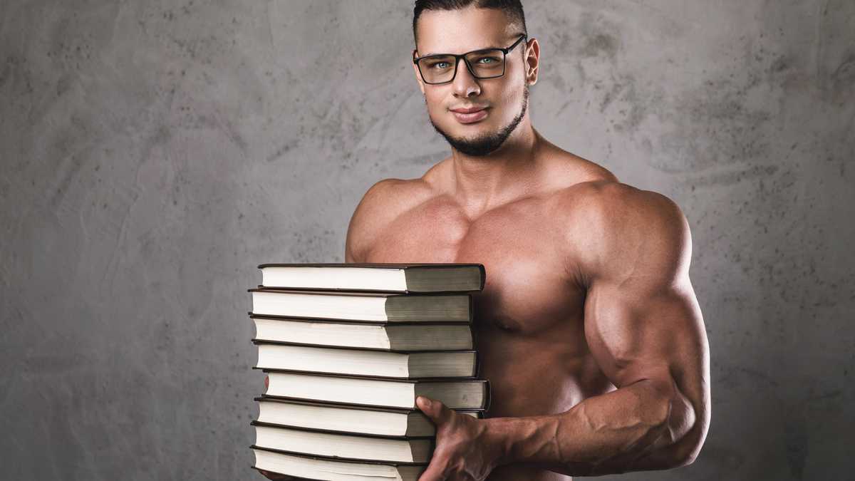 Smart and muscular man with a heap of books. Concept of knowledge in bodybuilding.