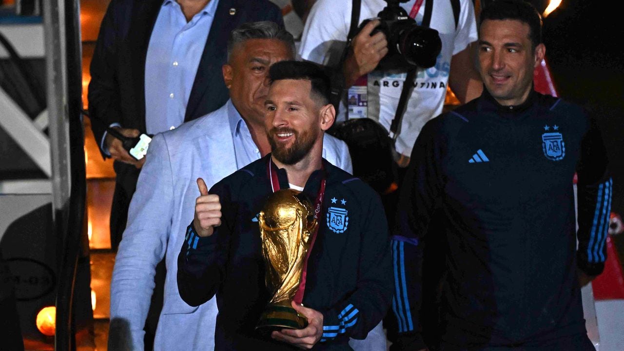 Argentina's captain and forward Lionel Messi (C) holds the FIFA World Cup Trophy alongside Argentina's coach Lionel Scaloni (R) upon arrival at Ezeiza International Airport after winning the Qatar 2022 World Cup tournament in Ezeiza, Buenos Aires province, Argentina on December 20, 2022. (Photo by Luis ROBAYO / AFP)