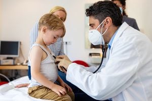 Doctor con mascarilla comprobando a un niño pequeño en su clínica. Pediatra examina al paciente niño con estetoscopio en la clínica. Covid