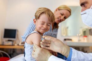 Niño frunciendo el ceño de dolor mientras recibe una vacuna en su brazo. Pediatra vacunando a un niño sentado con su madre en la clínica. covid