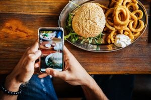 Un hombre tomando una foto de su hamburguesa artesanal con su teléfono inteligente antes de comerla.