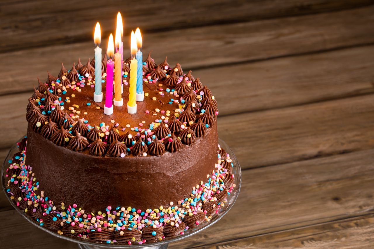 Pastel de cumpleaños de chocolate con chispitas de colores y velas sobre fondo de madera.