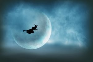 A witch flying on her broom across the sky is silhouetted in front of a large moon on Halloween night.