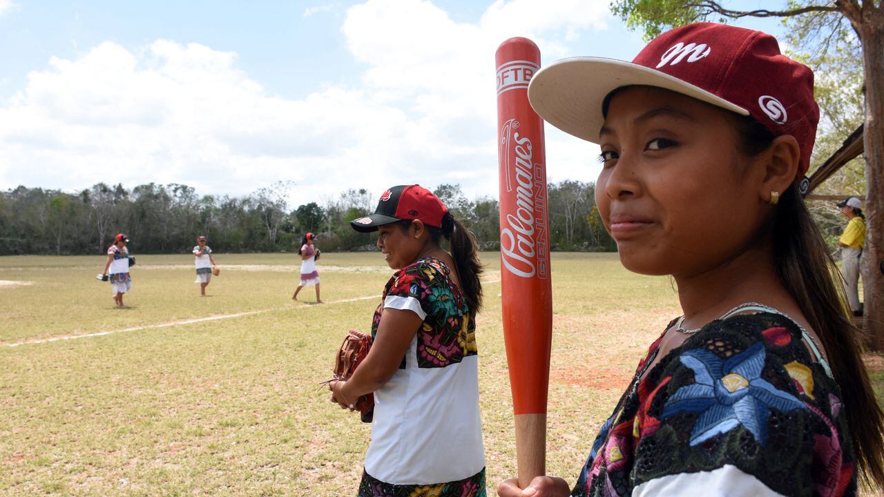 Players of "Las Diablillas de Hondzonot", wait for their turn to play during a softball match against "Guerreras de Piste", in Hondzonot, municipality of Tulum, Quintana Roo State, Mexico, on April 3, 2021. - Barefoot and in finely embroidered white dresses, a group of indigenous women leap onto the diamond. They are Las Diablillas de Hondzonot, a softball team that defies stereotypes in a community in southeastern Mexico. (Photo by ELIZABETH RUIZ / AFP)