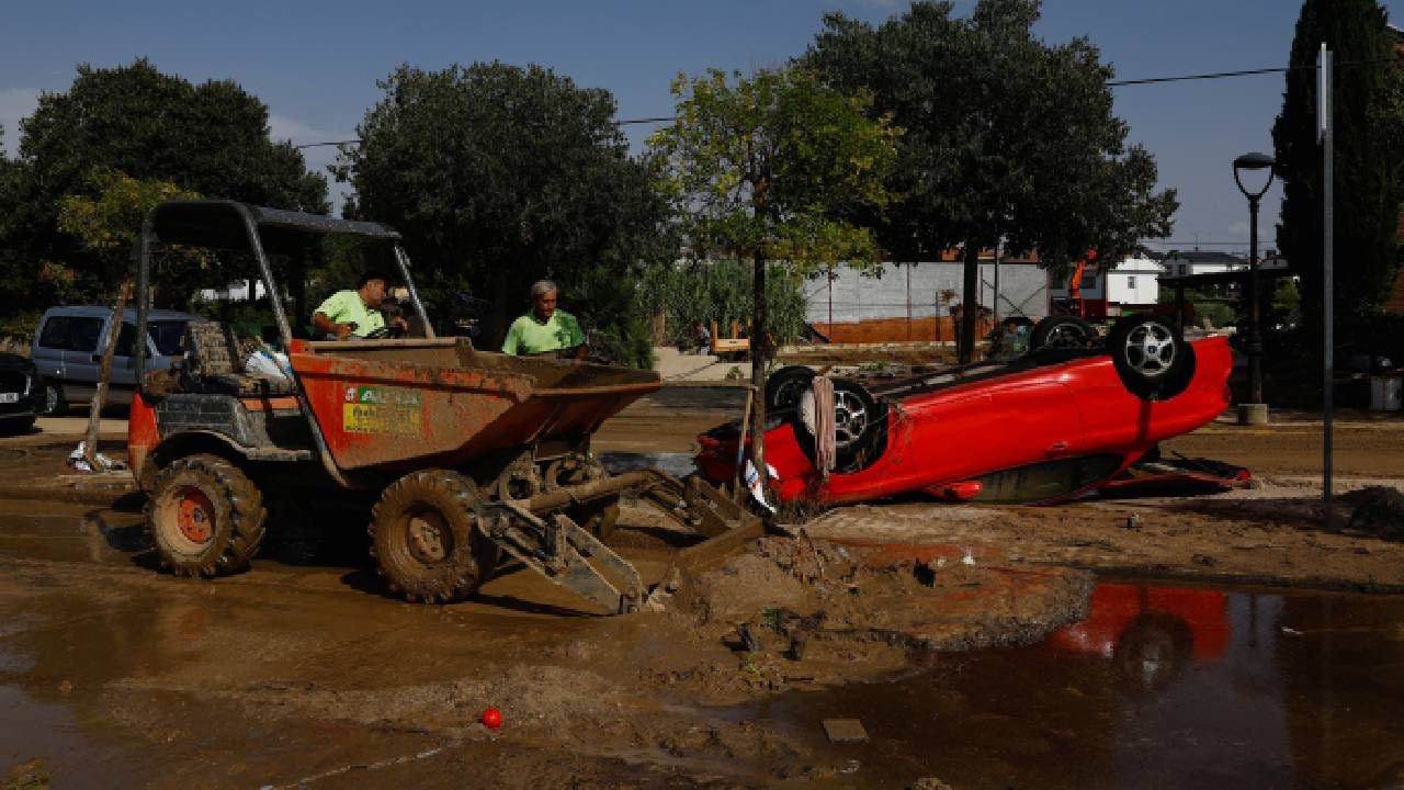 Los trabajadores retiran barro y escombros junto a un automóvil que fue volcado por fuertes lluvias, en El Álamo, España.
