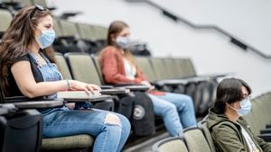 Grupo multiétnico de estudiantes que usan máscaras faciales protectoras mientras están sentados en una sala de conferencias a 2 metros de distancia.