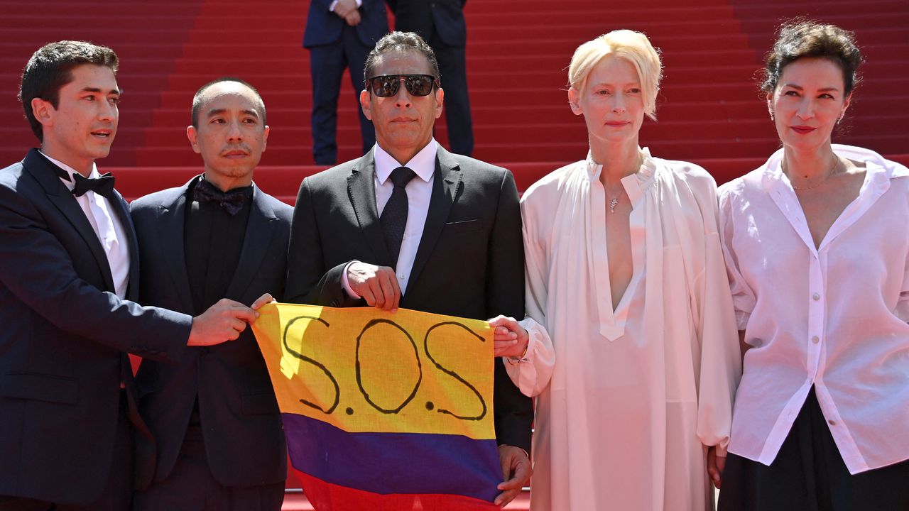 Juan Pablo Urrego, Apichatpong Weerasethakul, Elkin Diaz, Tilda Swinton y Jeanne Balibar con la bandera de Colombia que en el amarillo lanza el clamor urgente, "SOS". Se dio en el estreno de "Memoria" en la 74 Edición de Festival de Cine de Cannes.
