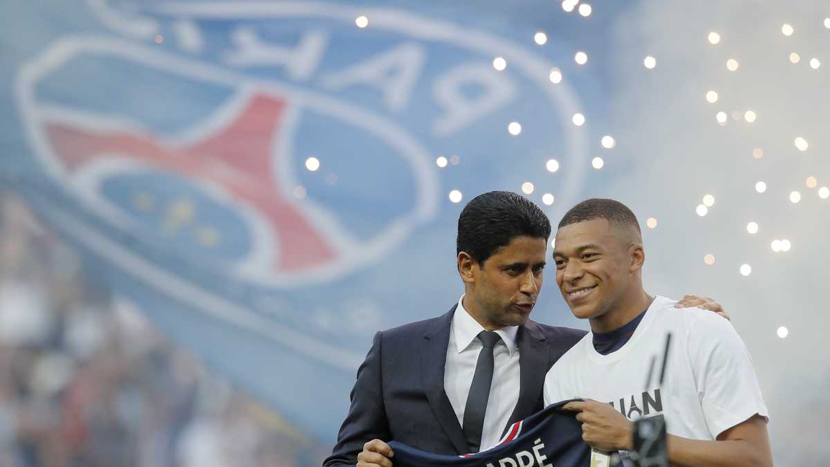PSG President Nasser Al-Khelaifi, left, speaks to PSG's Kylian Mbappe who holds a shirt with his name and 2025 on it as it is announced he has signed a three year extension to his contract on the pitch ahead of the French League One soccer match between Paris Saint Germain and Metz at the Parc des Princes stadium in Paris, France, Saturday, May 21, 2022. (AP Photo/Michel Spingler)