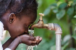 Niña africana bebiendo agua limpia de un grifo. Manos ahuecadas de un niño africano con agua saliendo de un grifo en las calles de la ciudad africana de Bamako, Malí.